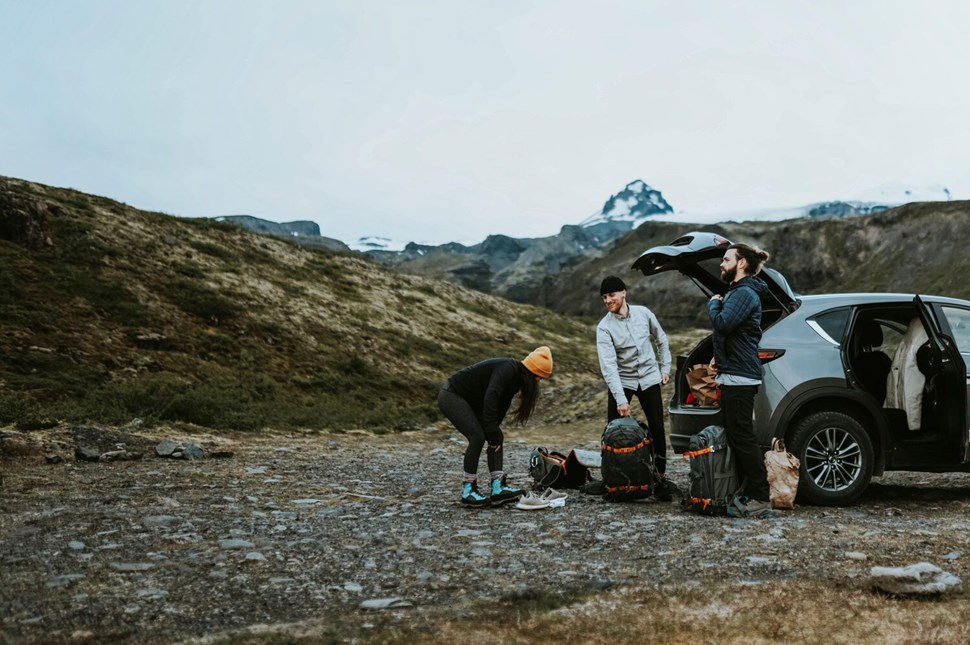 Group of travelers preparing gear beside their car on a gravel road with the rugged Icelandic terrain and distant mountains as a backdrop.