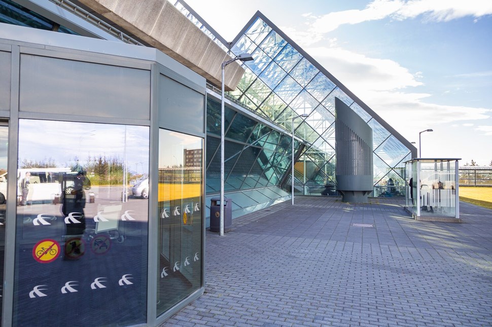 Glass facade of a building at Keflavik Airport with geometric designs, reflecting the bright sky and surroundings.