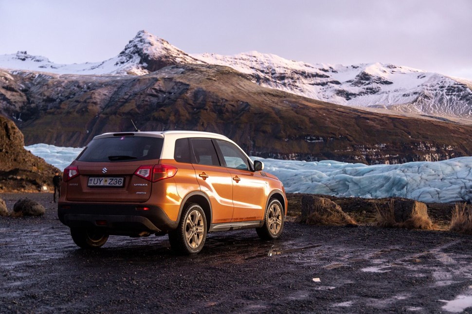 Orange SUV parked on a gravel road with a sprawling glacier and snow-capped mountains in the background in Iceland.