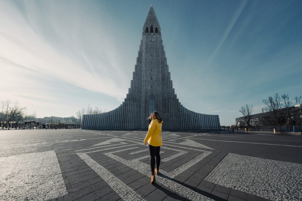 Person in a yellow jacket standing in front of the iconic Hallgrimskirkja church in Reykjavik, Iceland.