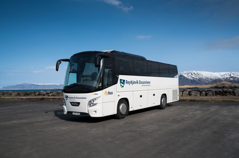 Flybus airport transfer bus parked with snow-covered mountains in the background in Iceland.
