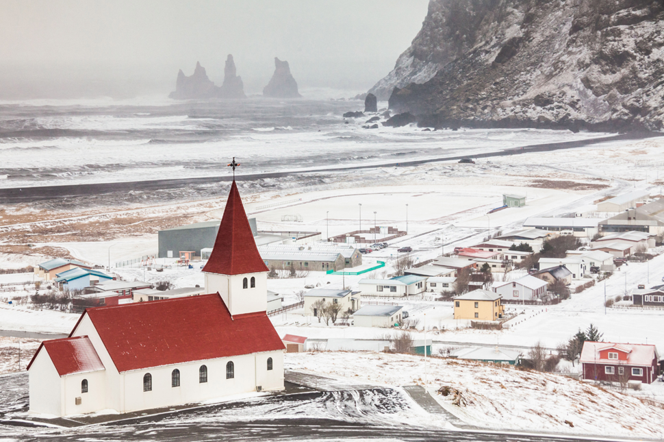 Red-roofed Vík church with snow covering the town.