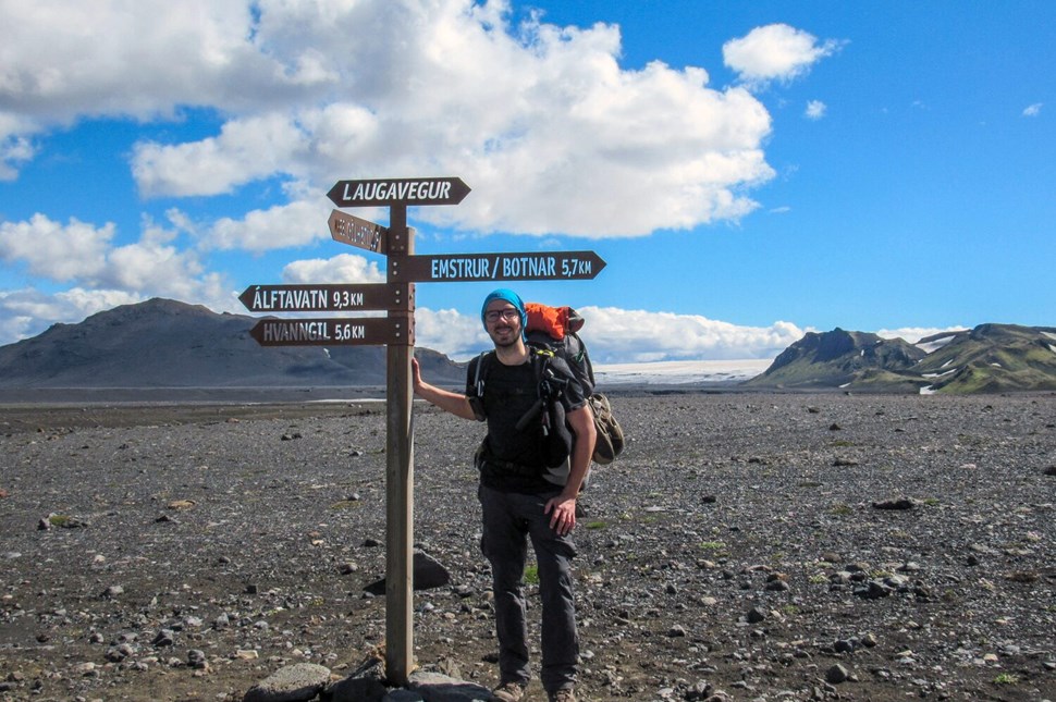Hiker posing by the Laugavegur trail road sign with different direction pointers.