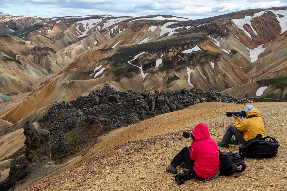 Travelers in red and yellow jackets sitting on the Laugavegur trail mountain slope.