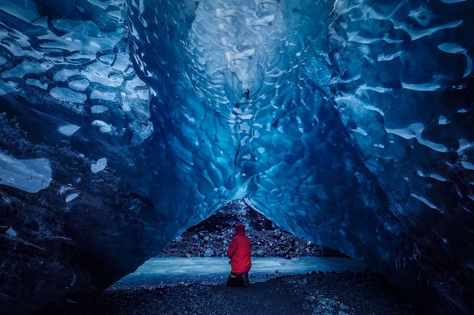 A person kneeling underneath the thick ice in a glacier cave