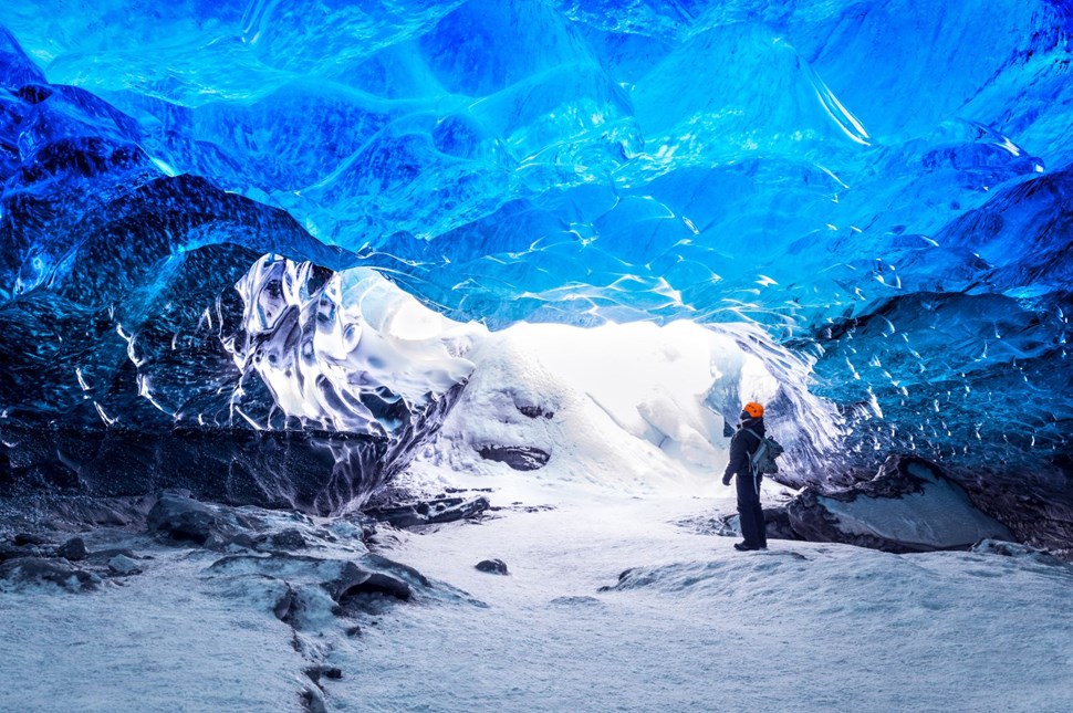 Man standing underneath the blue ice roof of an ice cave in Vatnajökull glacier