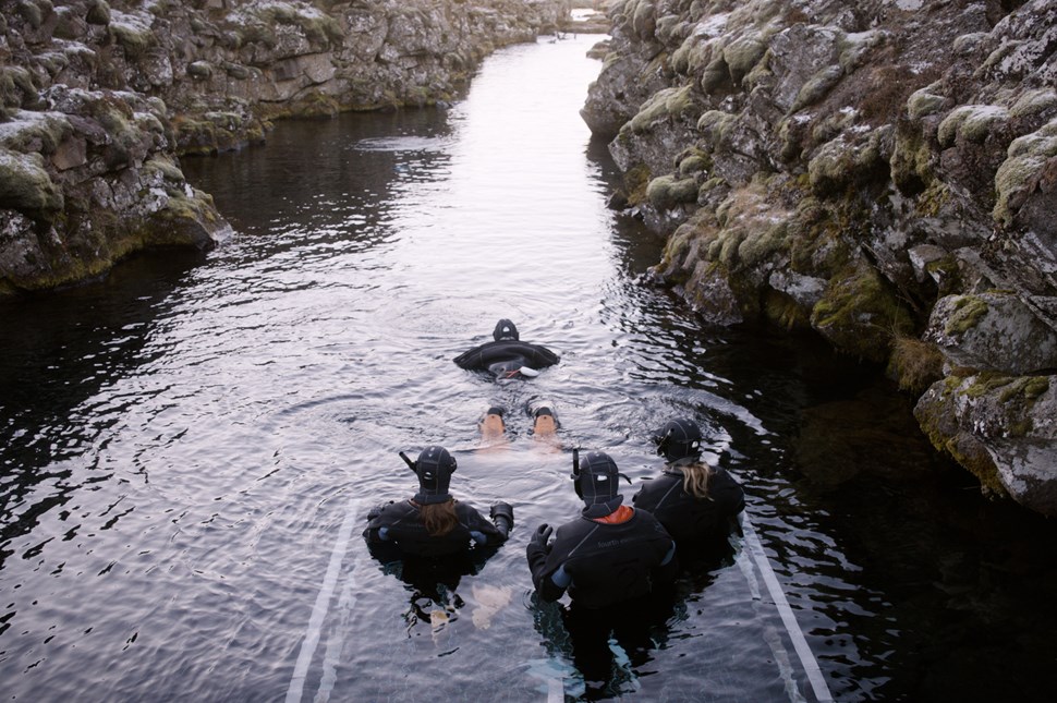 Snorkelers prepare to enter the water in a narrow, rocky channel.