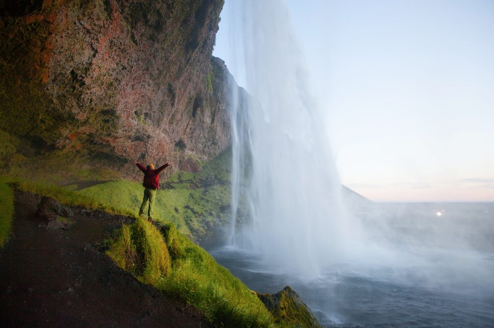 Woman Tourist Near The Seljalandsfoss Waterfall During The Sunset, Iceland