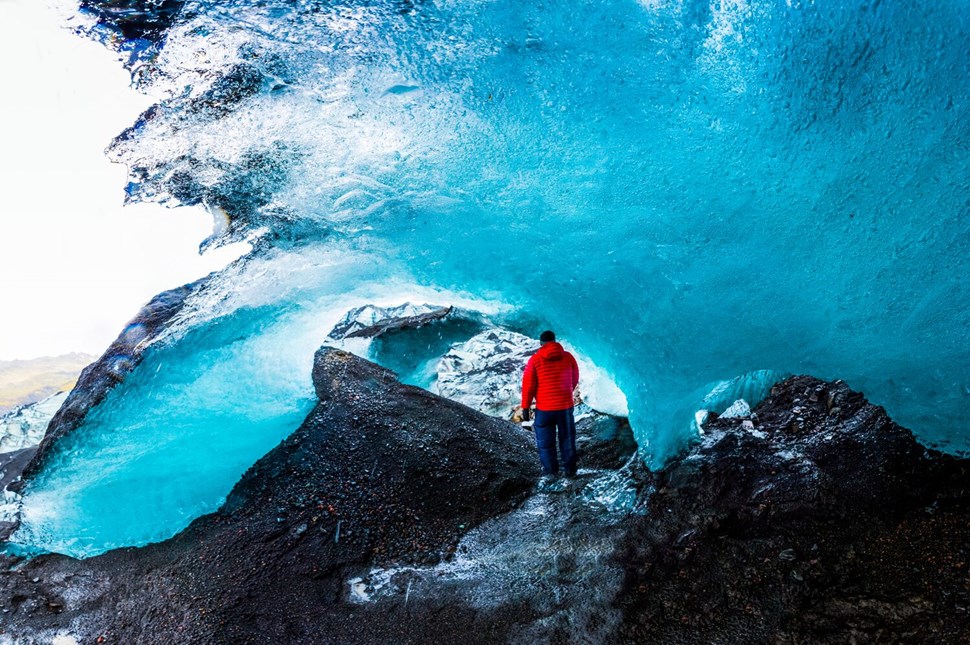 Tourist in red jacket standing inside the blue ice cave in Iceland