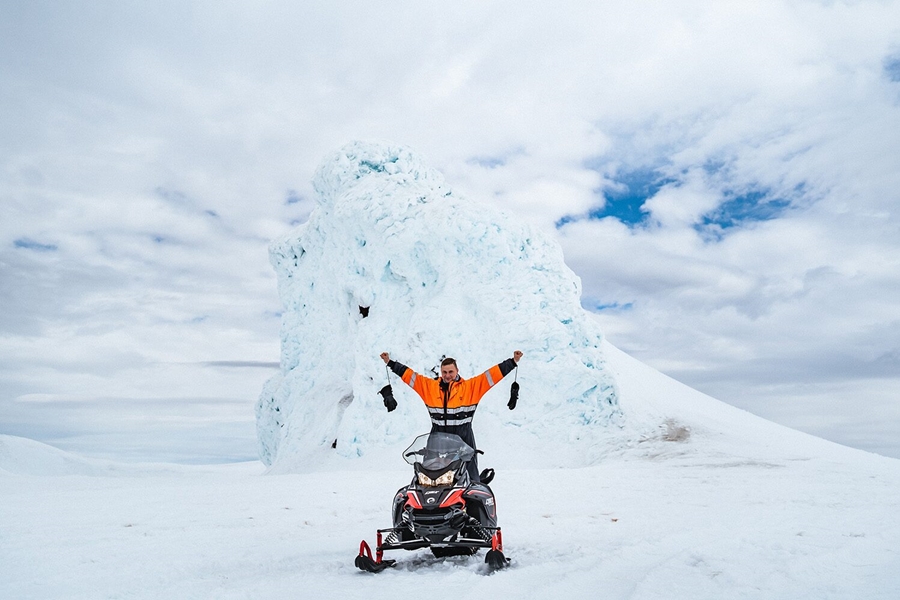 Man posing with snowmobile on glacier