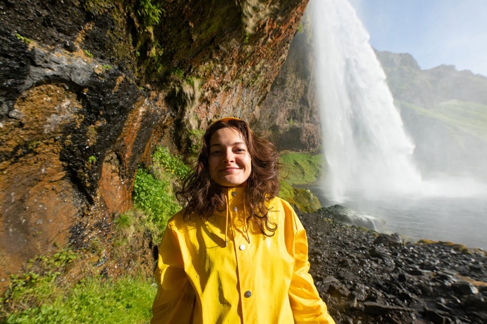Woman with yellow jacket posing by waterfall