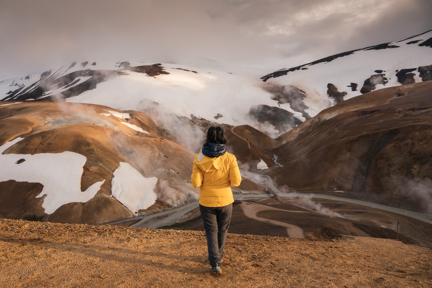 Woman looking over fuming terrain with snowy mountains
