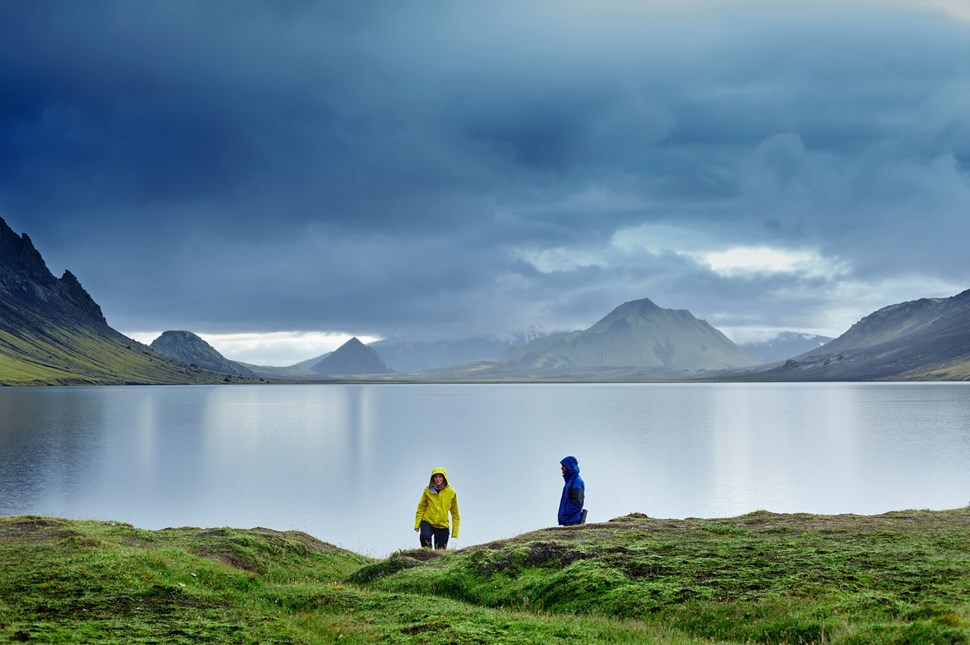Two people at distance on backdrop of Icelandic lake & mountains