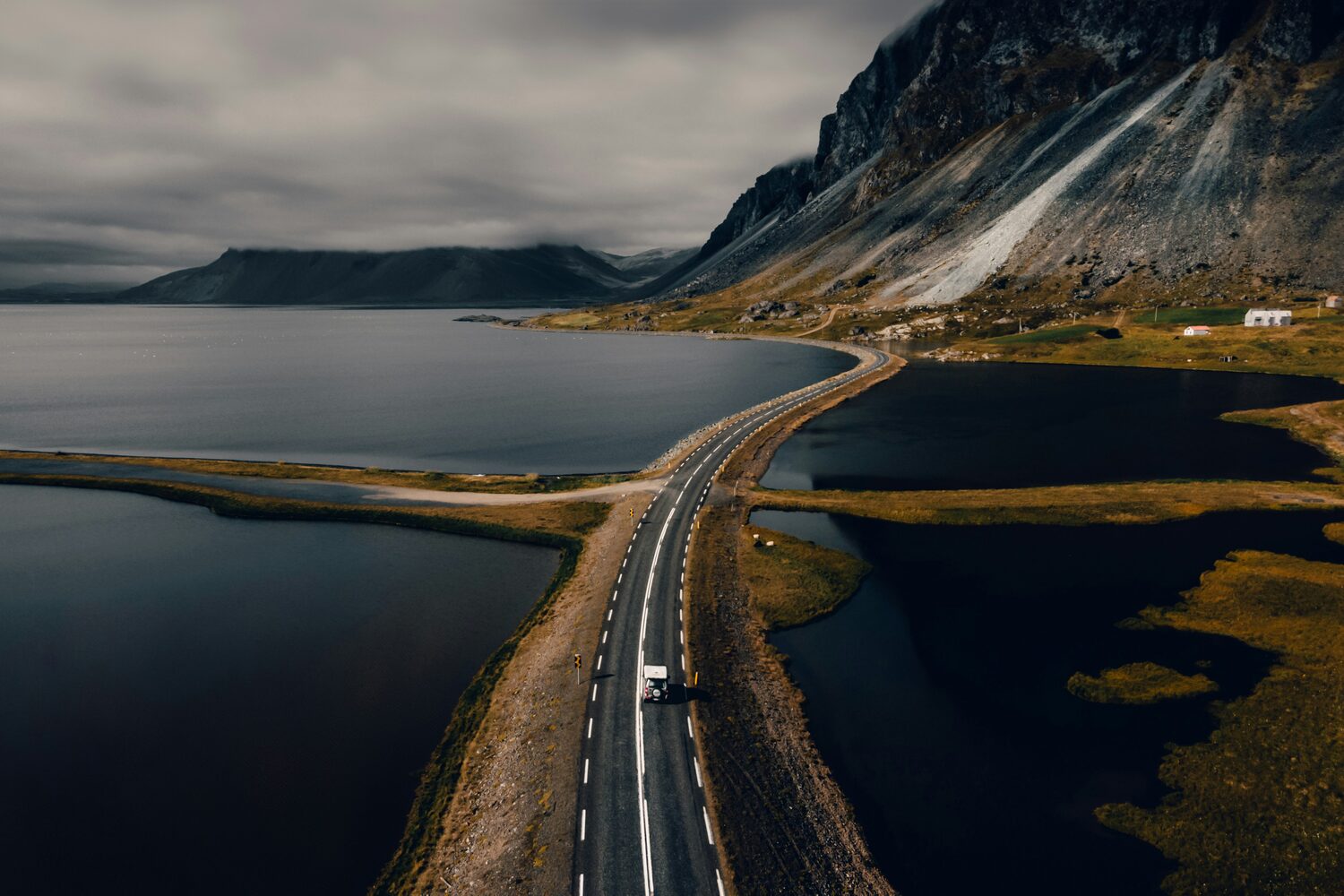 Ariel shot of bridge of road driving over the sea next to mountain and low clouds in Iceland