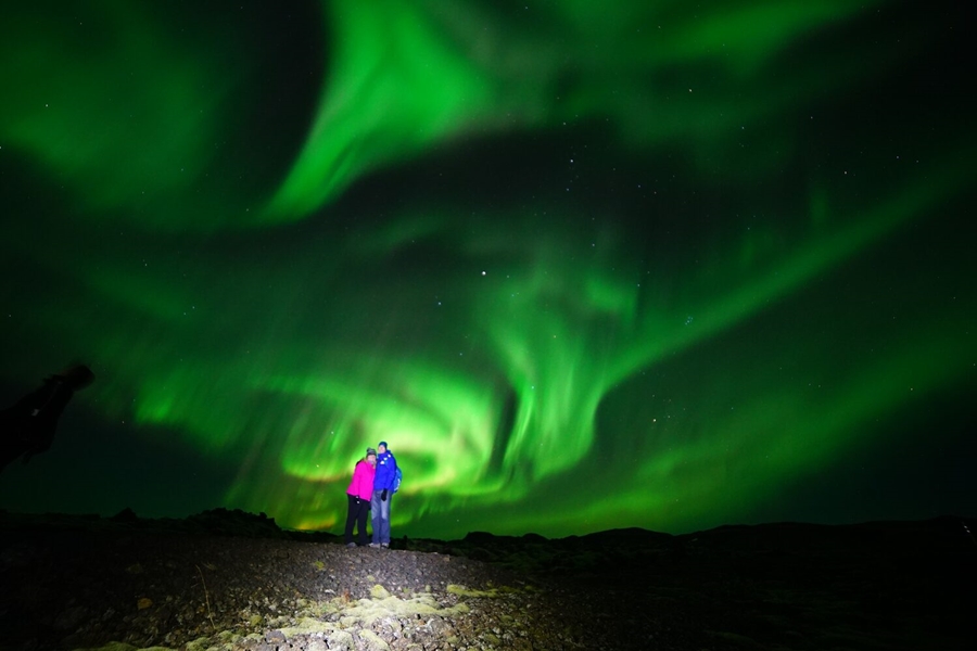 Couple posing for photo with Northern lights above