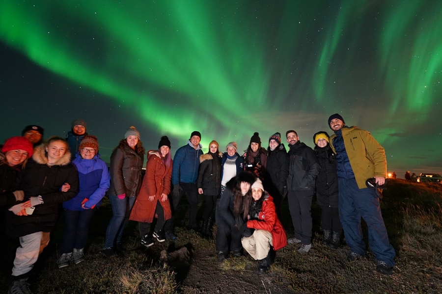 Big group of people posing for photograph with northern lights above