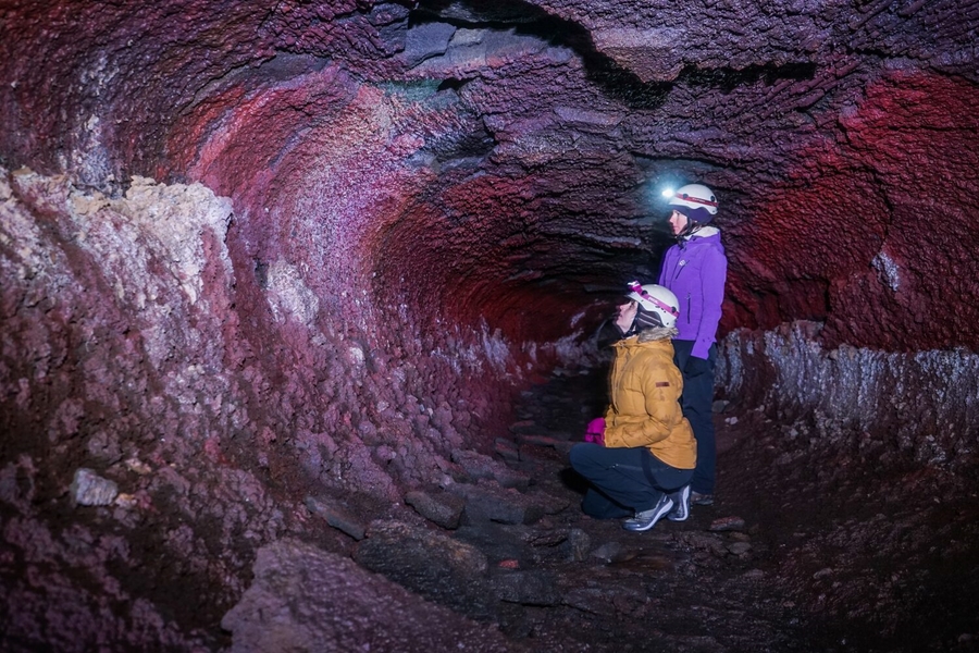 Two women exploring lava cave with headlamps