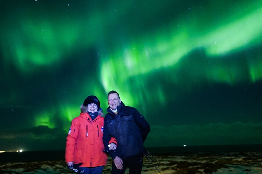 Couple smiling for photo with aurora in the sky