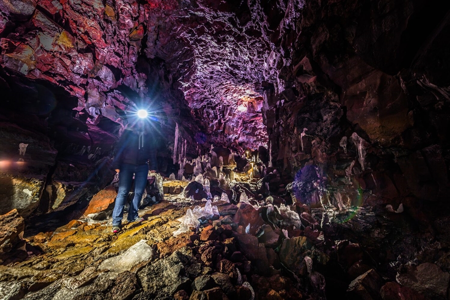 Man with headlight in huge pink lava tube