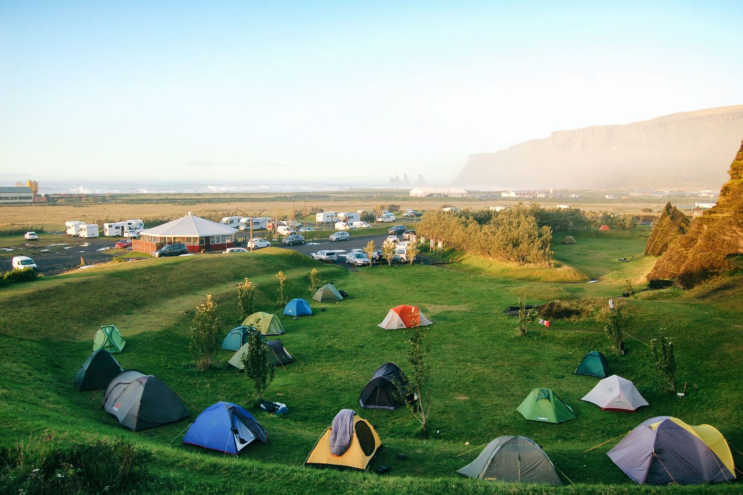 Colorful tents set up in bright green field, camping ground with mountain in horizon.