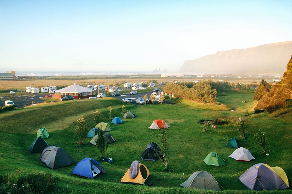 Colorful tents set up in bright green field, camping ground with mountain in horizon.