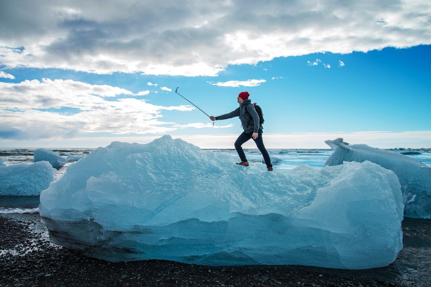Tourist with red hat standing on iceberg, taking selfie at diamond beach, Iceland. 