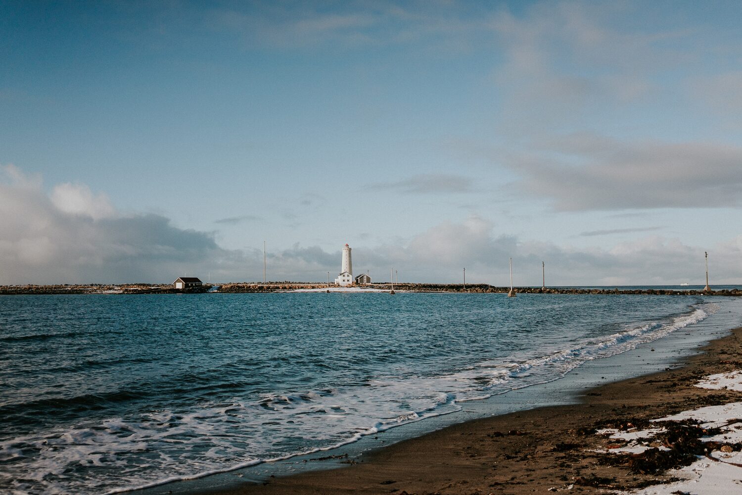 Grotta beach in Iceland, shore with waves and white lighthouse in the background and cloudy skies.