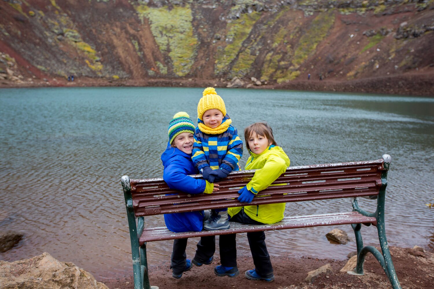 Three children sitting on bench at Kerid volcanic crater lake in Iceland.