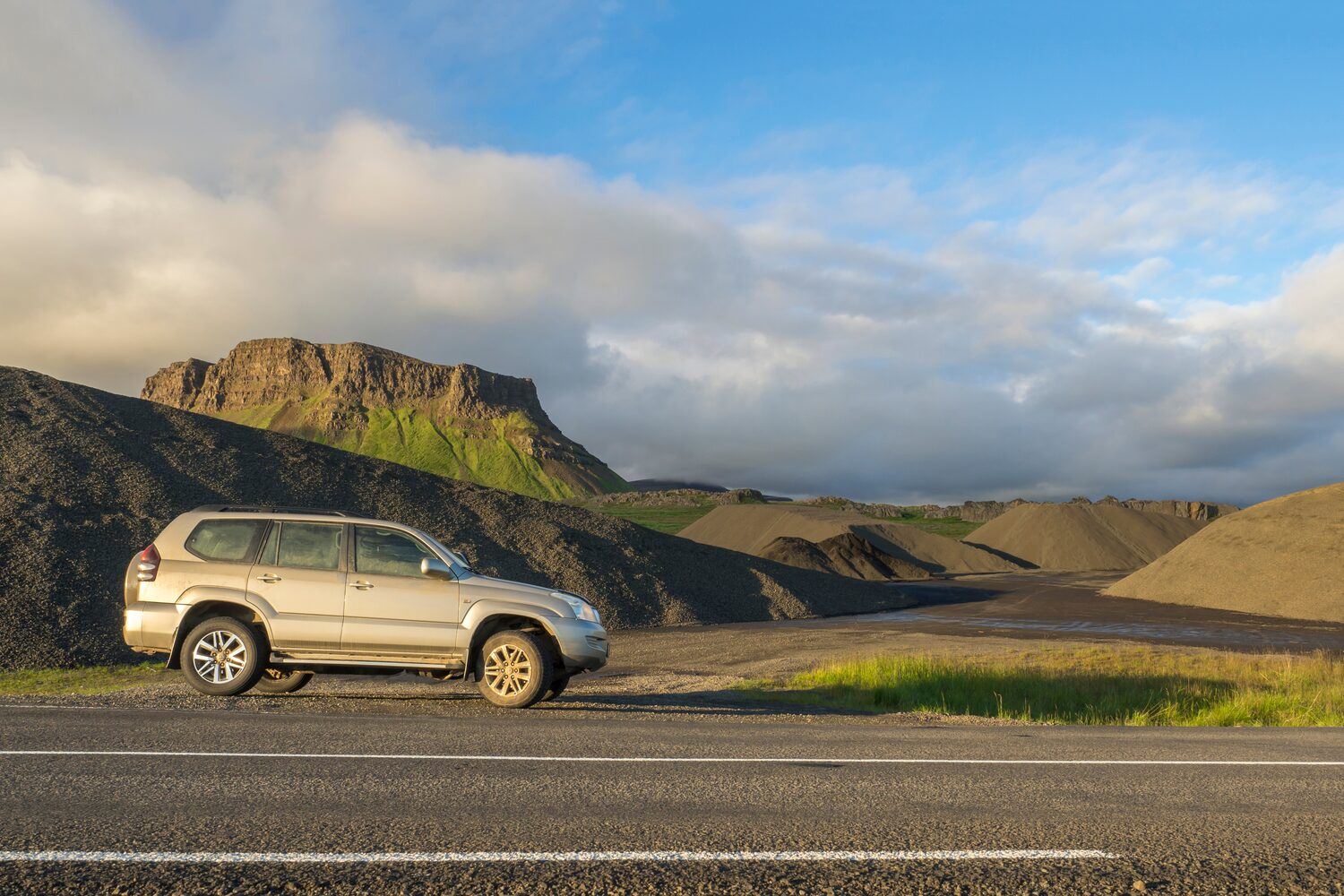 Grey Toyota Land Cruiser Prado parked infront of mountain in scenic Iceland countryside.