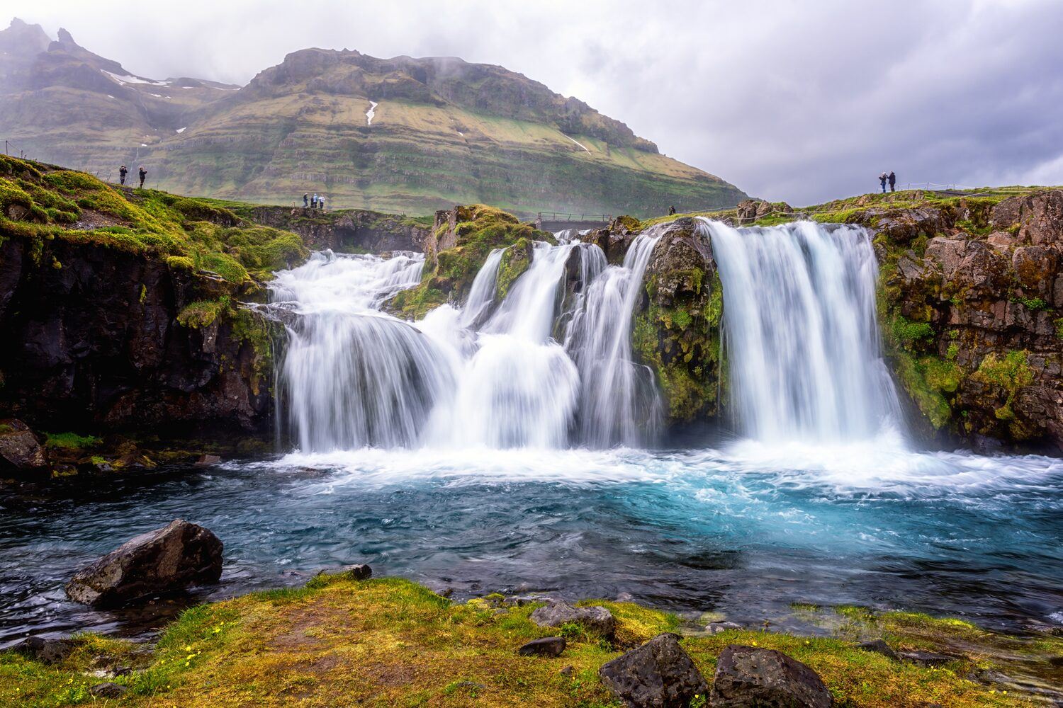 Kirkjufellsfoss waterfall with tourists standing around the edge admiring.