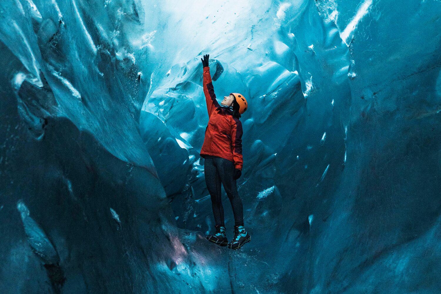 Tourist in red jacket and safety hat in ice cave in Iceland.