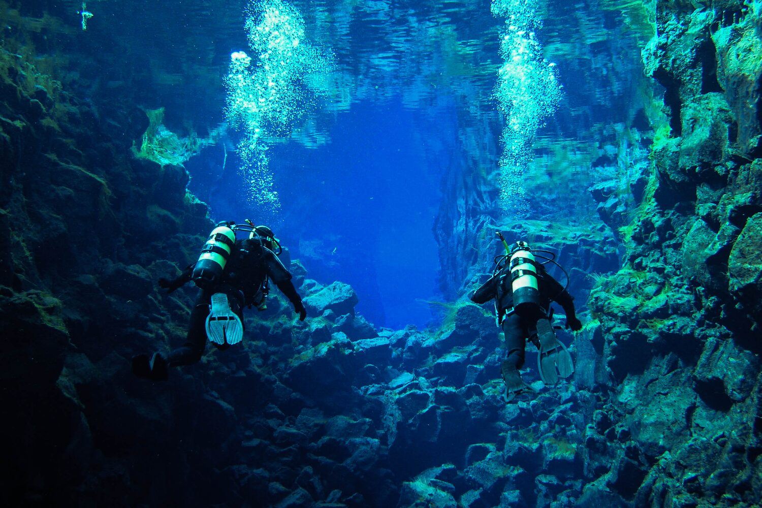 Two divers in deep blue waters of Silfra Thingvellir in Iceland.