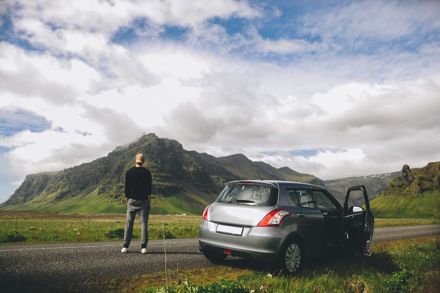 Man looking out to a mountain in Iceland, next to car on road from a scenic route.