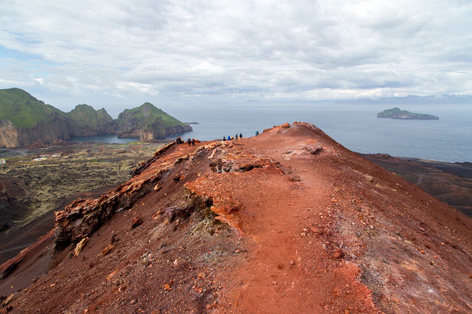 Red volcanic ash at Blick vom Vulkan Eldfell, with tourists hiking on top.