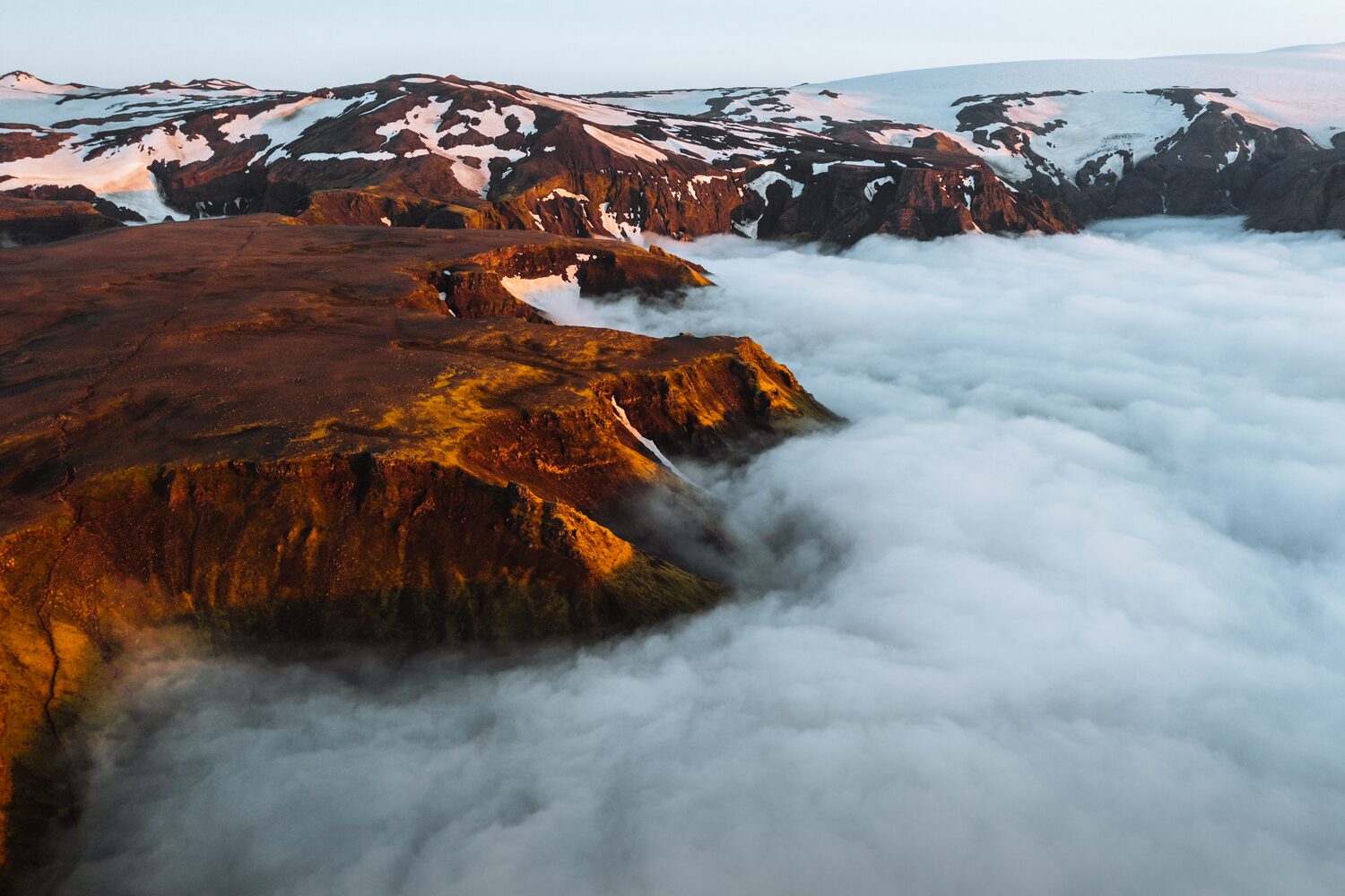 Mountain top surrounded by thick clouds with snowy mountains in background.