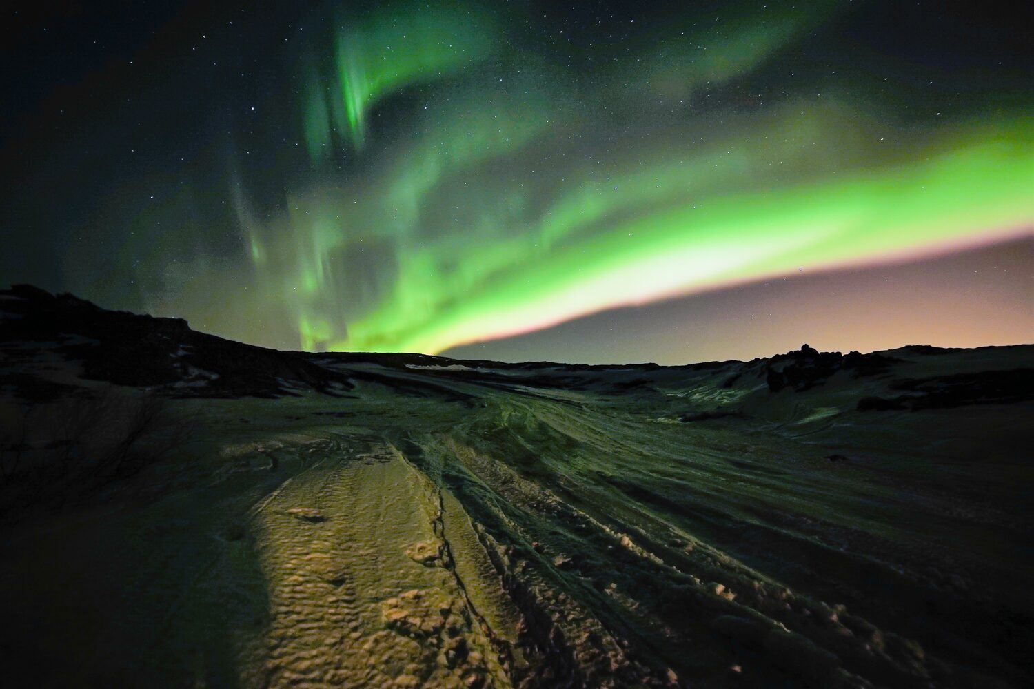 Bright green and purple wavy northern lights shining their light over the snow in Iceland