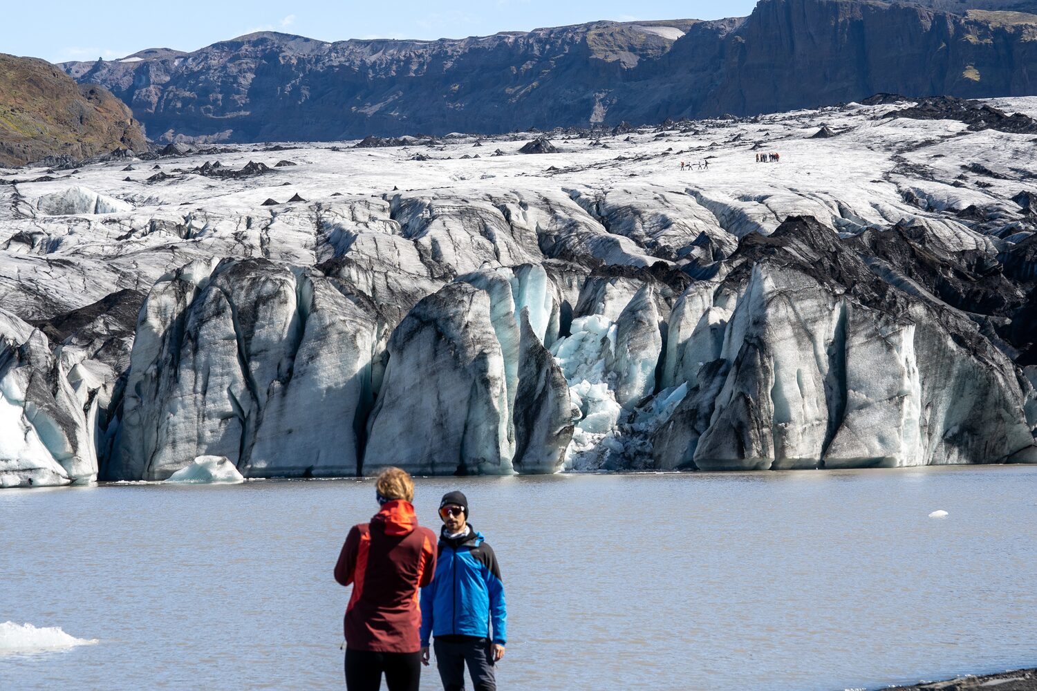 Two tourists standing at solheimajokull by snowy cliffs and sea water