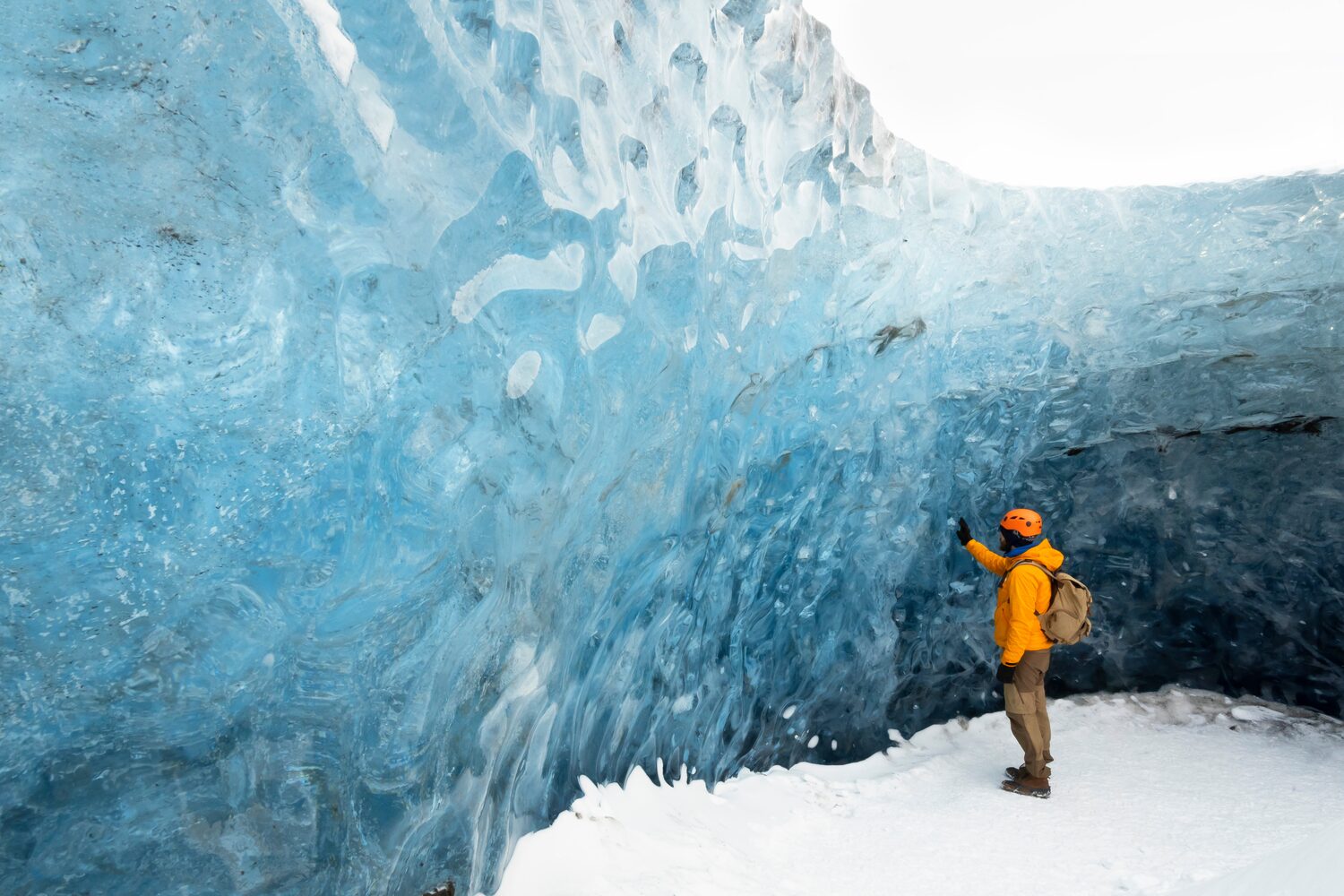 Man by blue glacier ice wall in Iceland