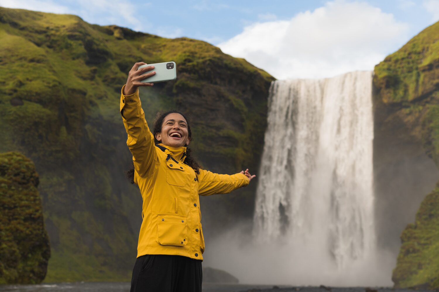 Woman in yellow jacket taking selfie by waterfall