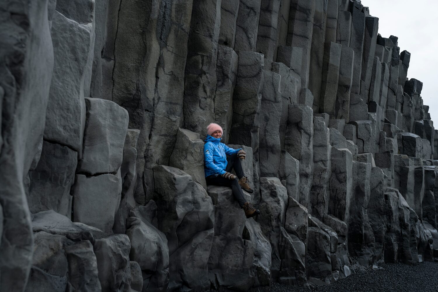 Tourist sitting on stacked rock cliff at Southcoast Black Sand beach in Reynisfjara