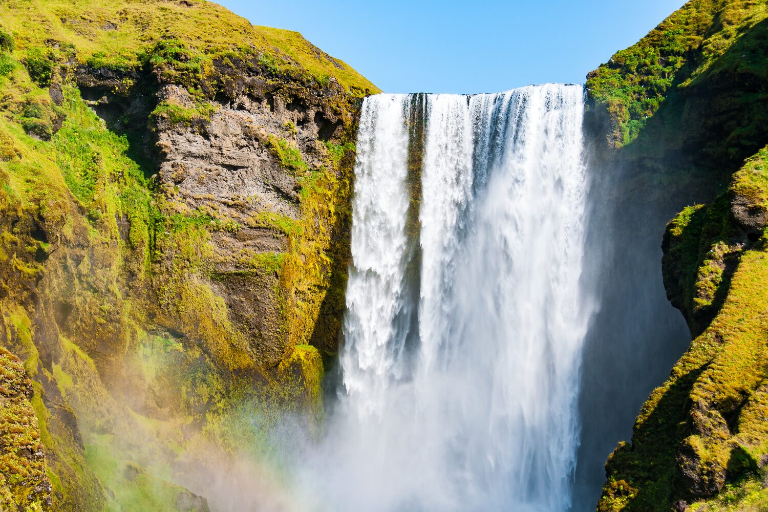 Close up view of yellowy green moss covered rock cliff with waterfall fast flowing