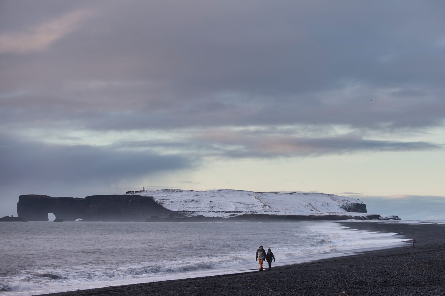 Couple walking on the black sand beach shore