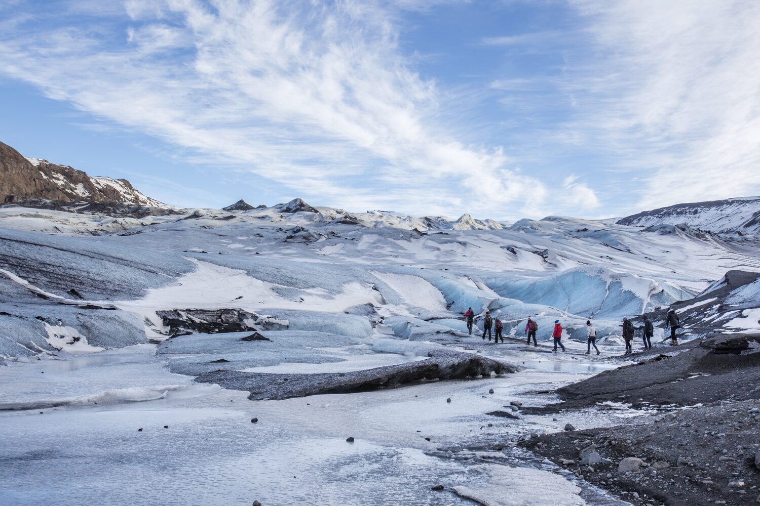 Tourists forming a line walking across a glacier route blue sky with clouds 