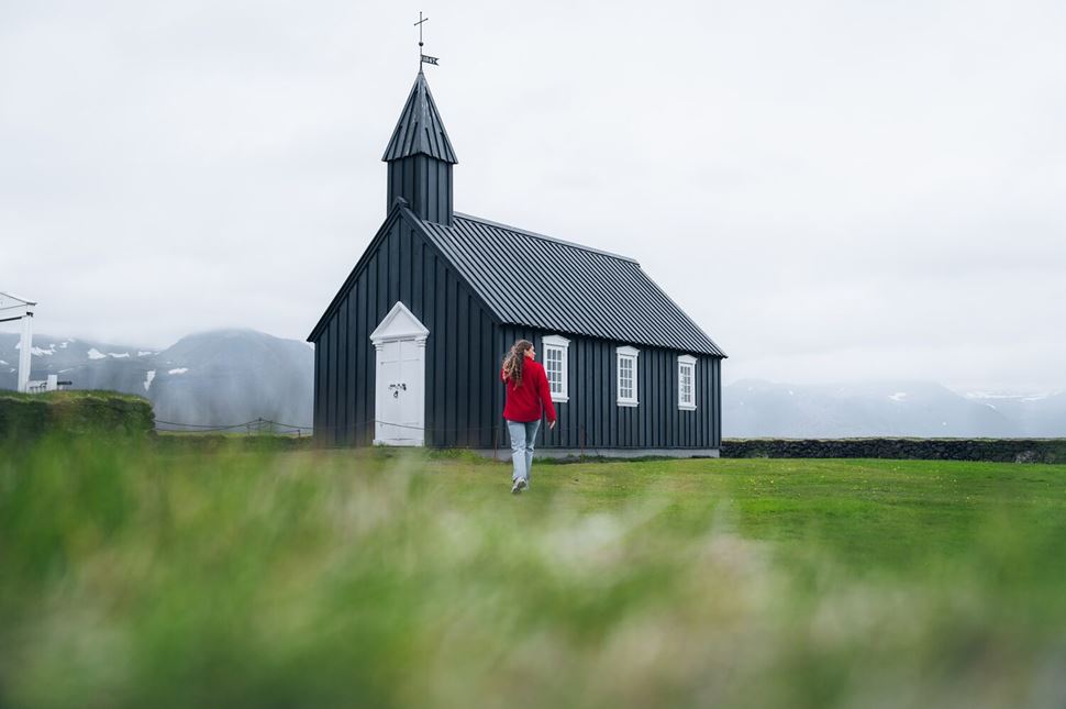 Woman by black church Woman with red sweater by black church in Iceland