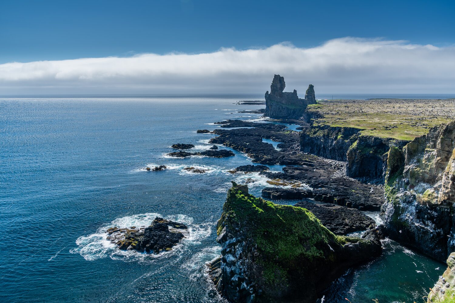 Rocky cliff next to deep blue sea, basalt towers resembling castle