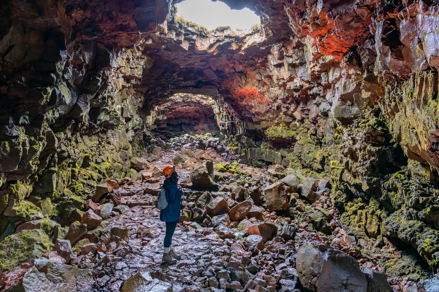 Lady walking inside lava tunnel with colored lava rock