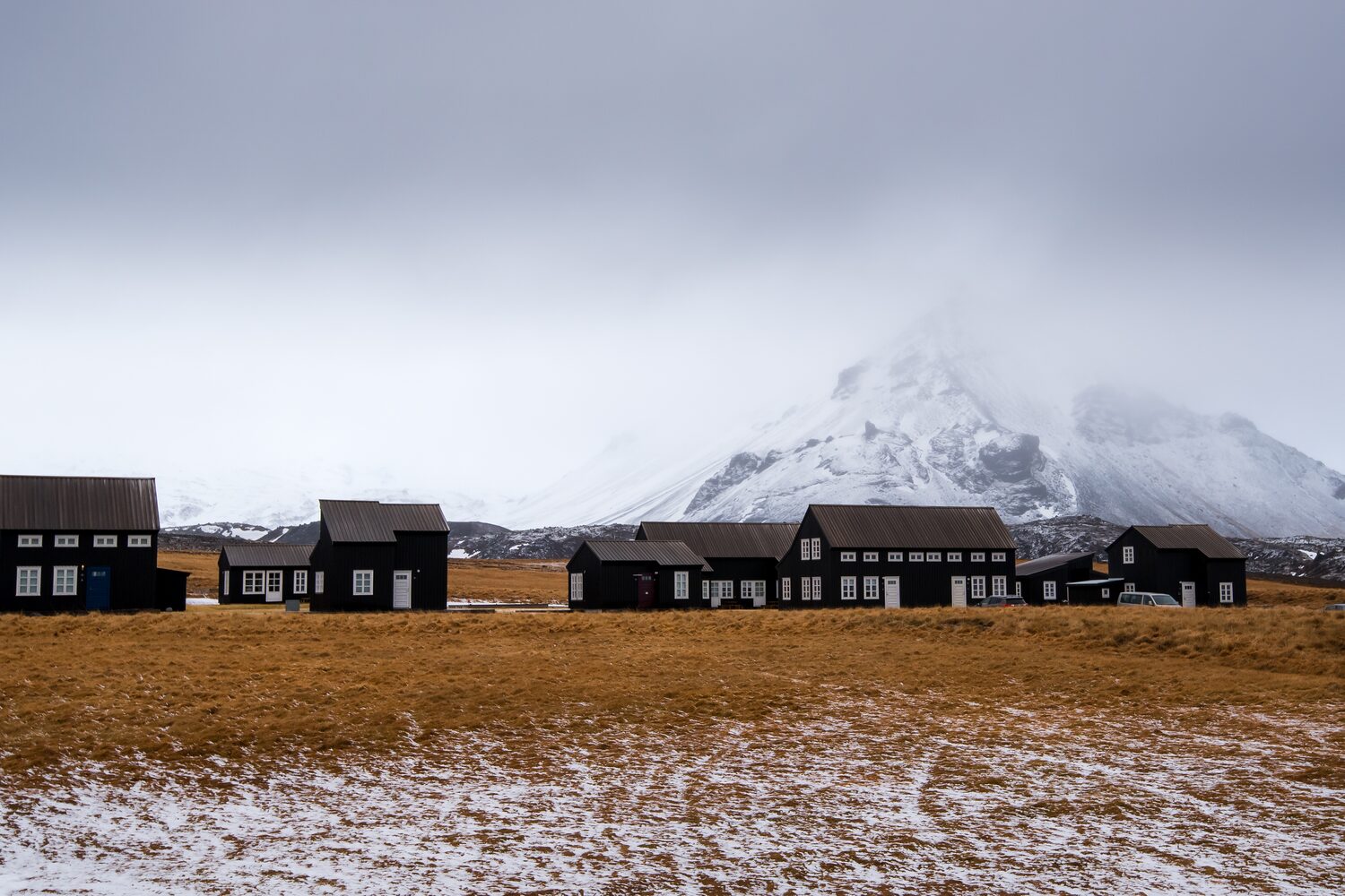 Small brown houses in front of snow capped mountain and white misty sky 