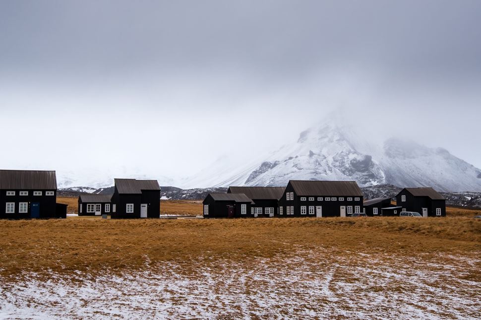 Fishing Village Hellnar Small brown houses in front of snow capped mountain and white misty sky