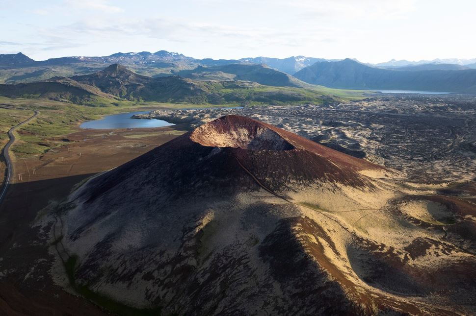 Landscape of volcanic crater The view of a volcanic crater in a dark brown color, green mountains in the background and a lake.