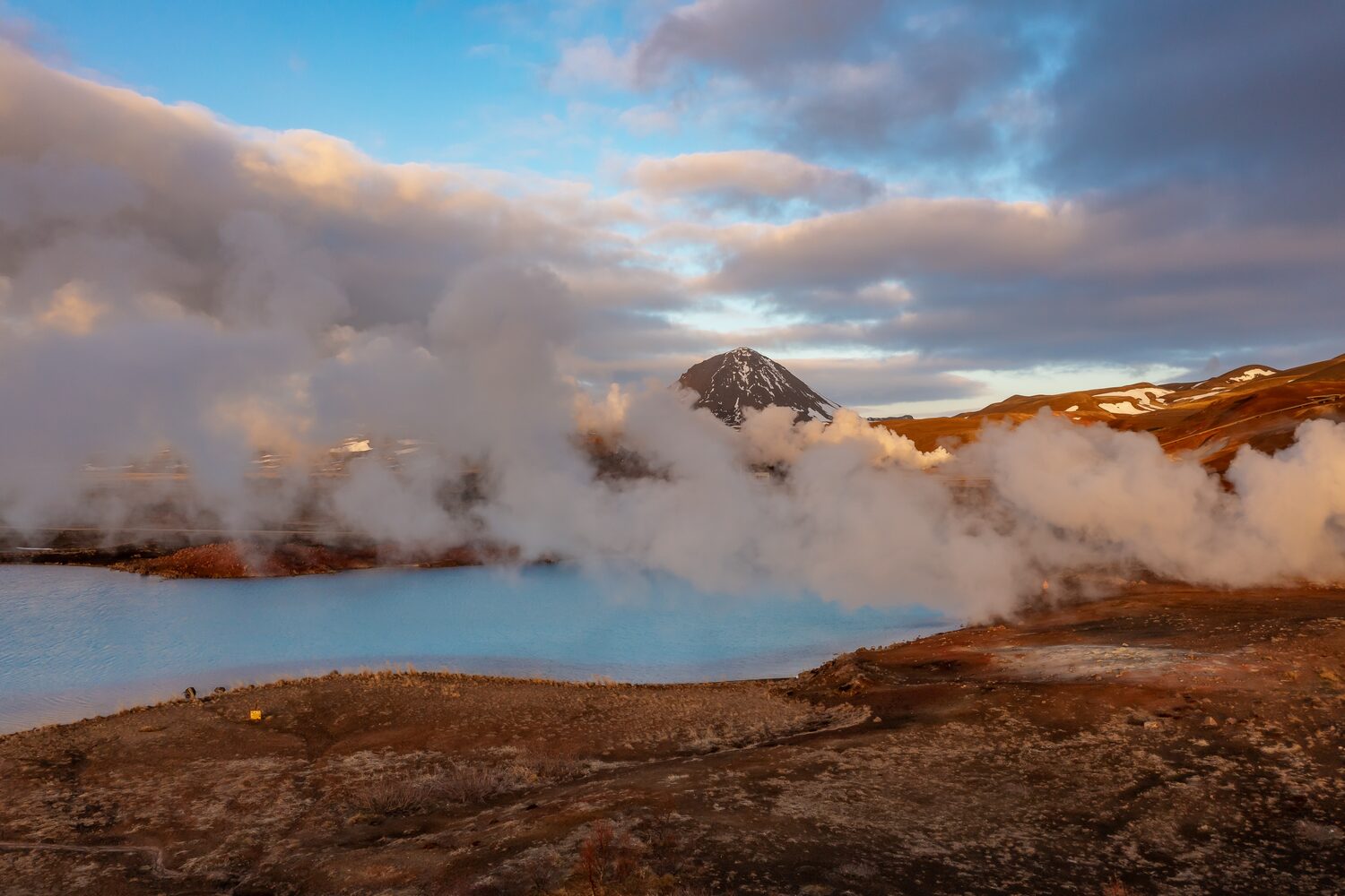 Cloudy sunset drone view of frozen lake on swamps on mountain hills with smoke in sky from geothermal activity